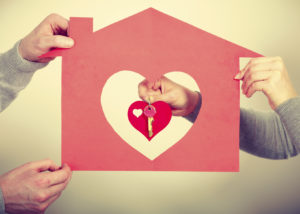 Key to happiness and living together. Love and dream. Woman hand holds little red heart with keys to new home house flat apartment holding by man.