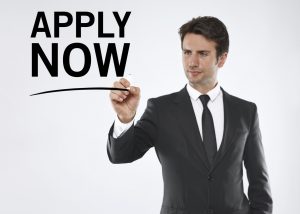 Businessman writing "Apply now" on a clipboard.